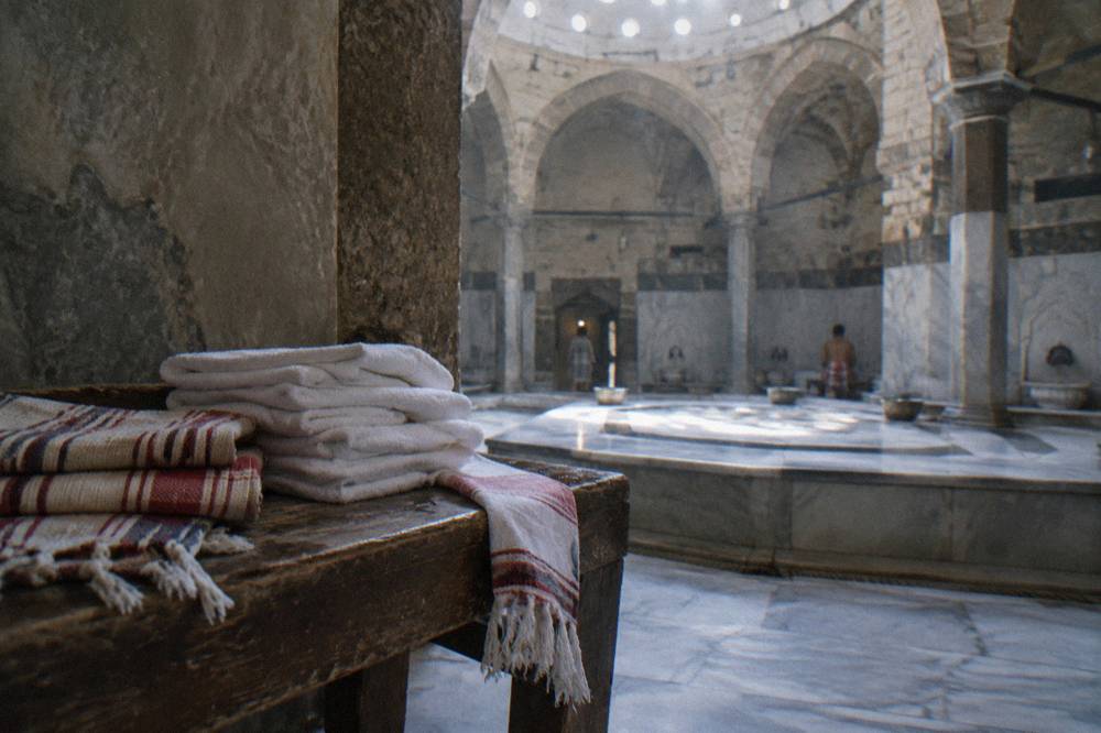 Folded white towels and woven cloths stacked on a wooden hamam bench