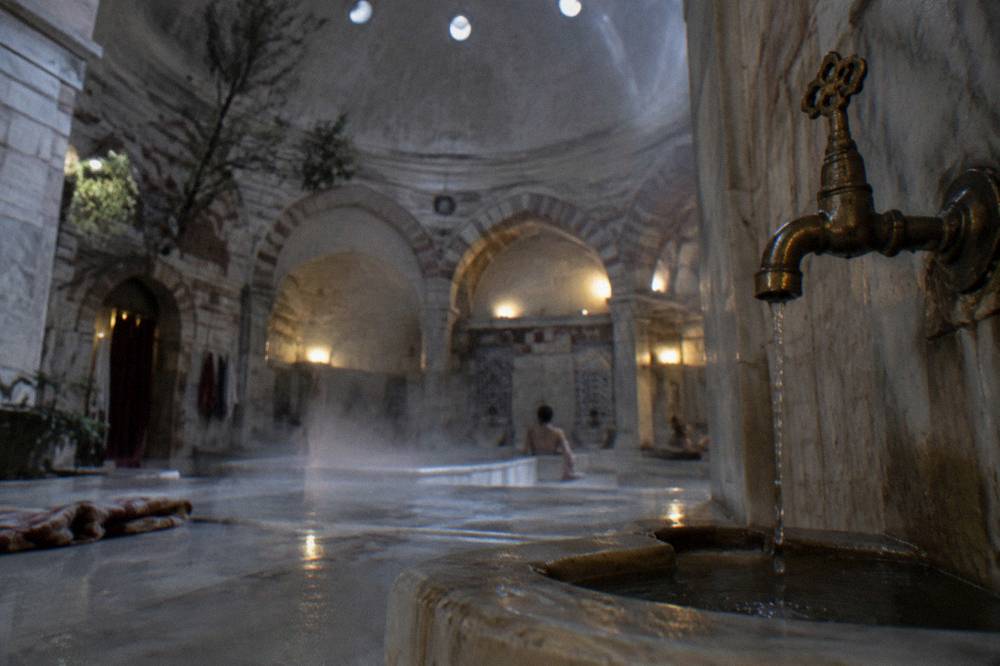 Steam rising from a heated marble slab in a domed hammam lit by small ceiling openings