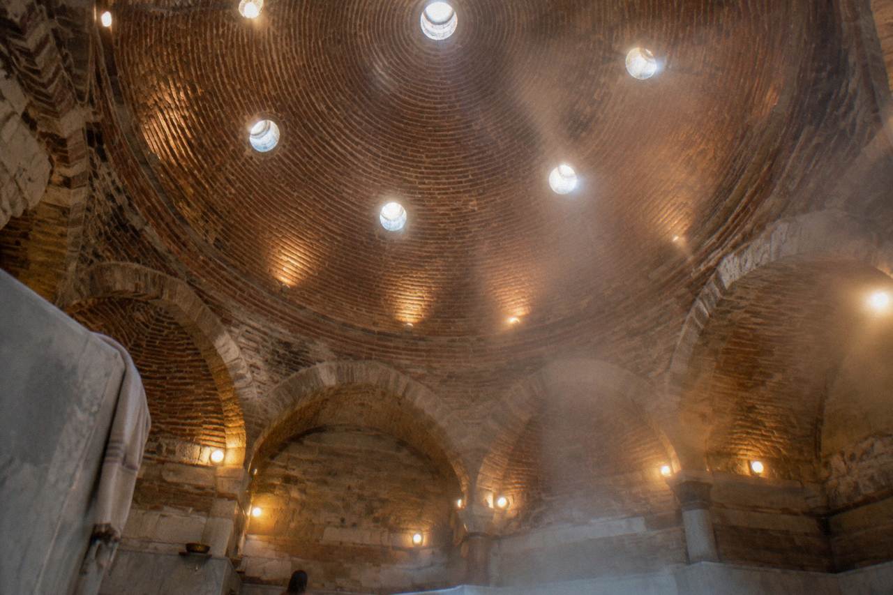 Domed ceiling of an Ottoman bathhouse with small round glass lights casting warm reflections on stone