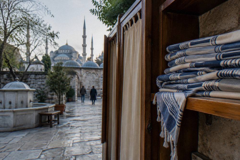 folded striped peştemal wraps stacked on a wooden shelf beside a hamam changing cabin