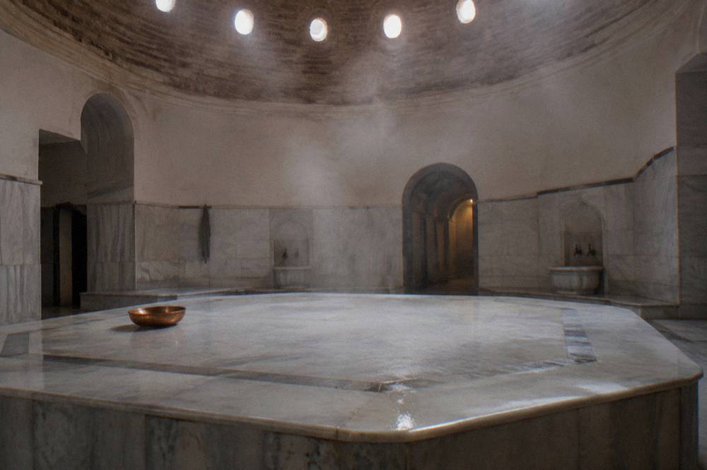 steam rising under a domed ceiling above an empty marble platform in a hamam hot room