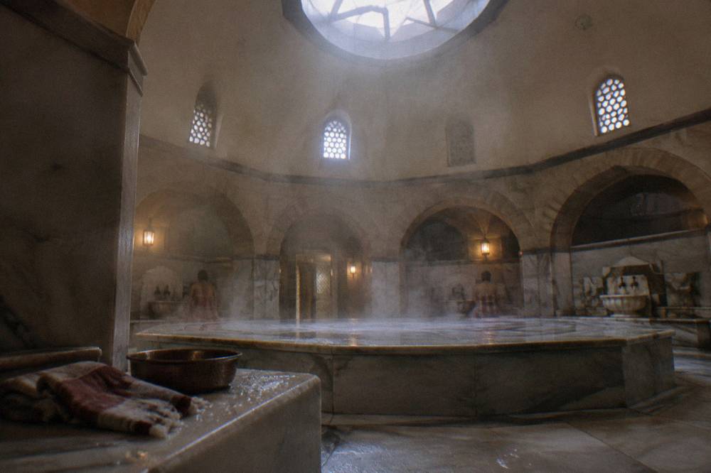 Warm marble göbektaşı platform in a domed hamam with steam lit by roof light