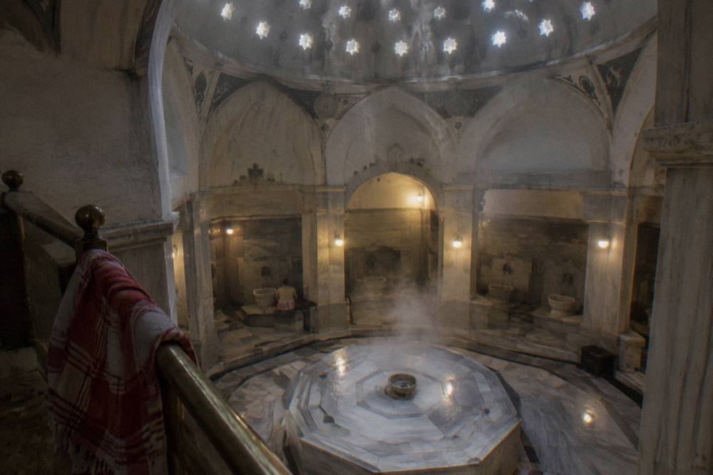 Steam rising from a heated marble platform beneath a domed hamam ceiling set with glass lenses