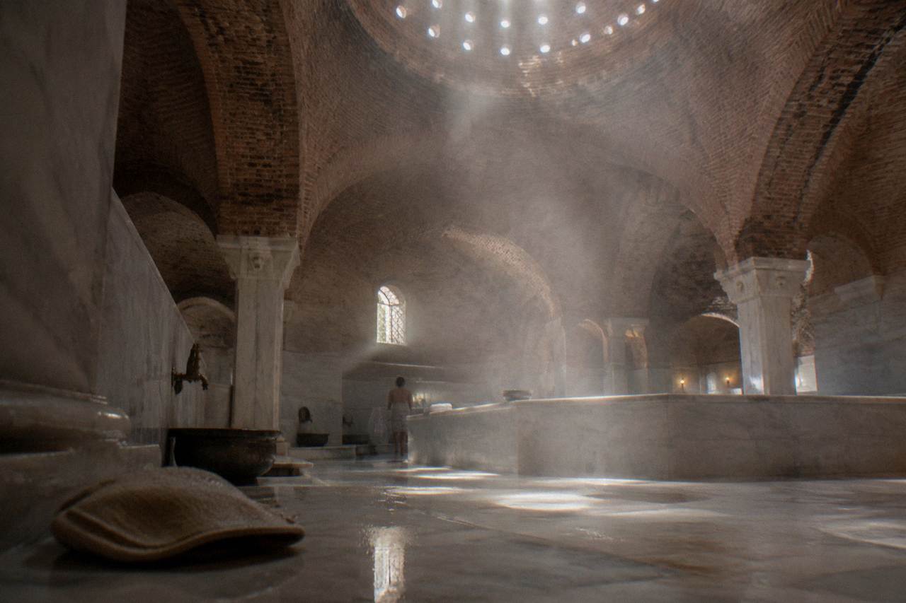 Steam drifting under the domed ceiling of an Ottoman hamam above a heated marble floor