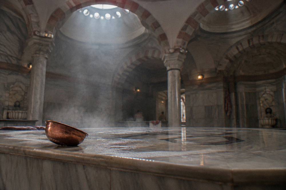 Heated marble gobektasi platform in a steamy hammam room lit through ceiling domes