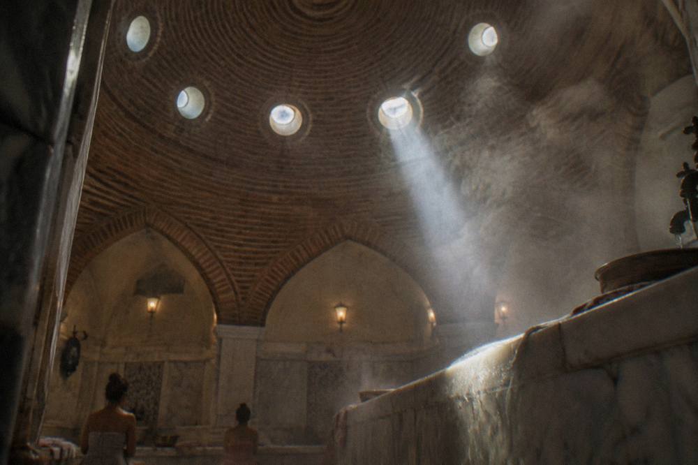 Domed hamam ceiling with circular glass lights casting beams onto drifting steam