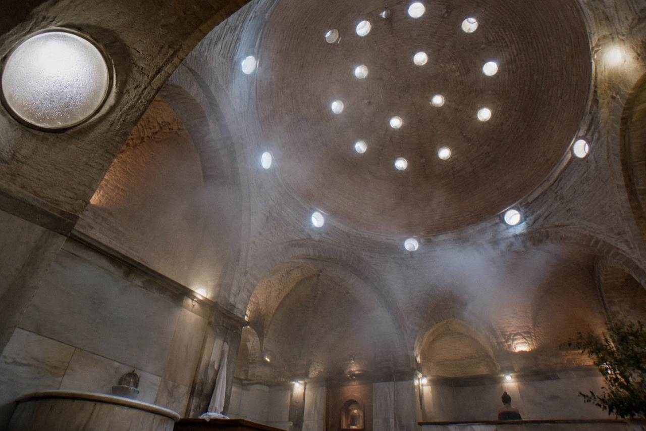 Domed hamam ceiling with small round glass lights and steam drifting across warm stone