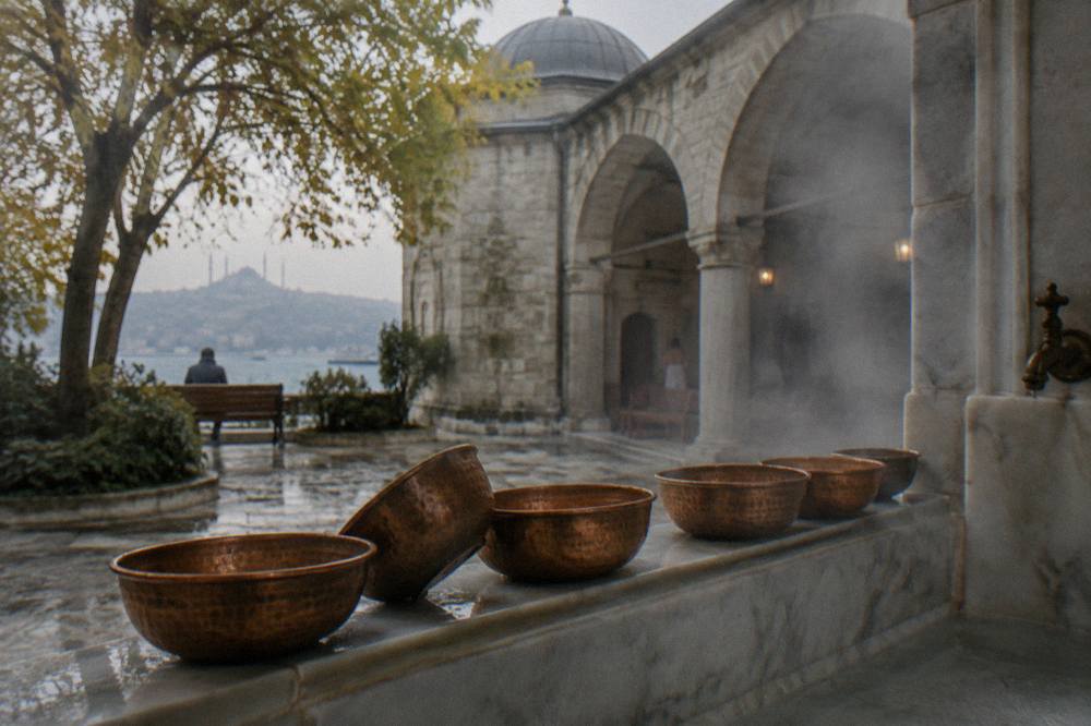 Copper bowls and a marble basin along the wall of a steamy hamam