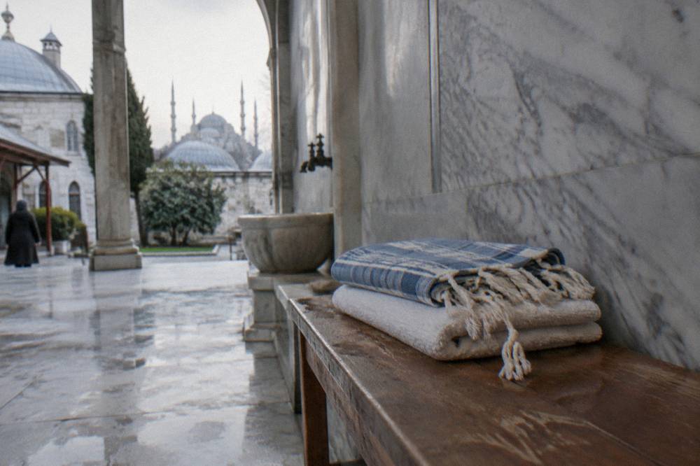 A folded peştemal cloth and stacked towels on a wooden bench beside a marble wall