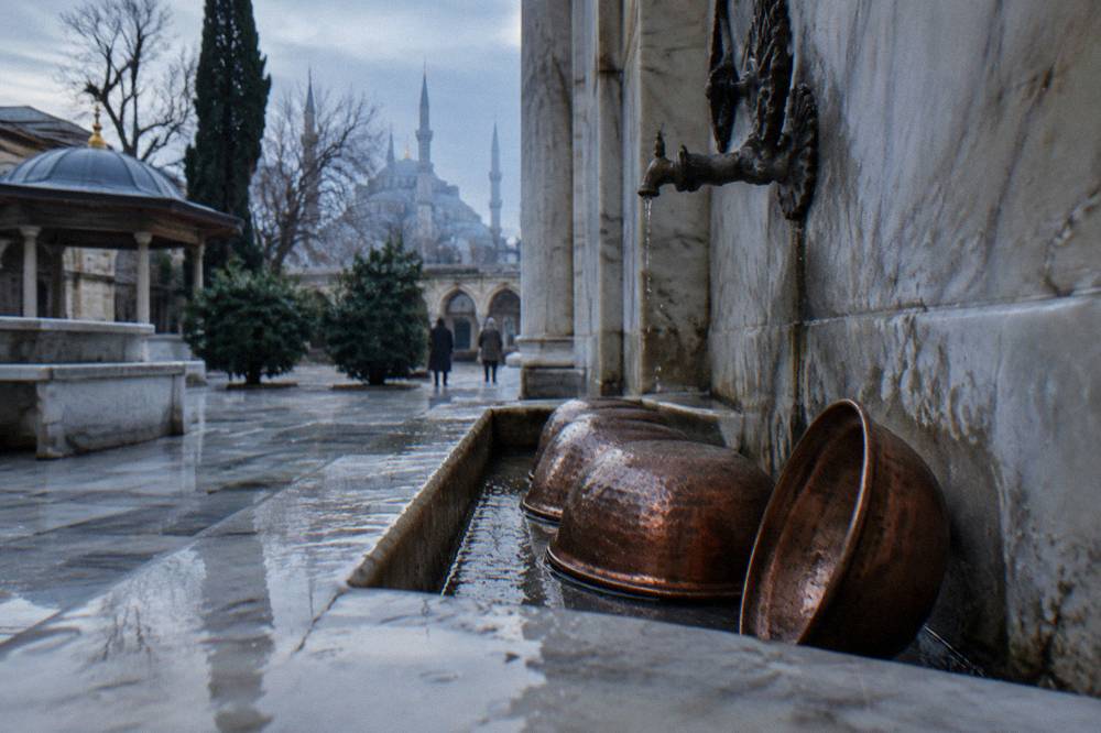 Copper bowls and marble basins along the wall of a hammam washing area