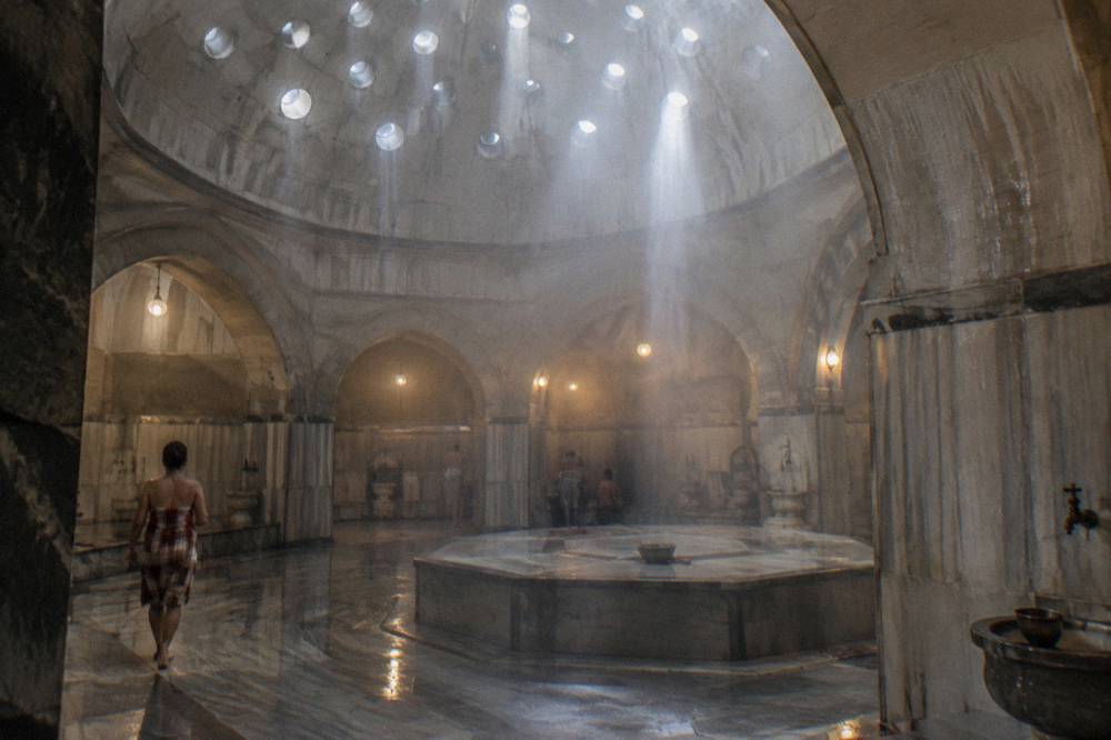 Domed hamam ceiling with small round glass lights casting warm beams onto marble floors