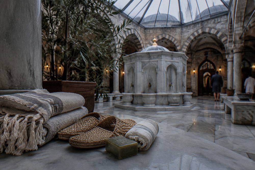 Folded towels, slippers, olive oil soap and a cotton wrap arranged on a marble bench inside a Turkish bath.