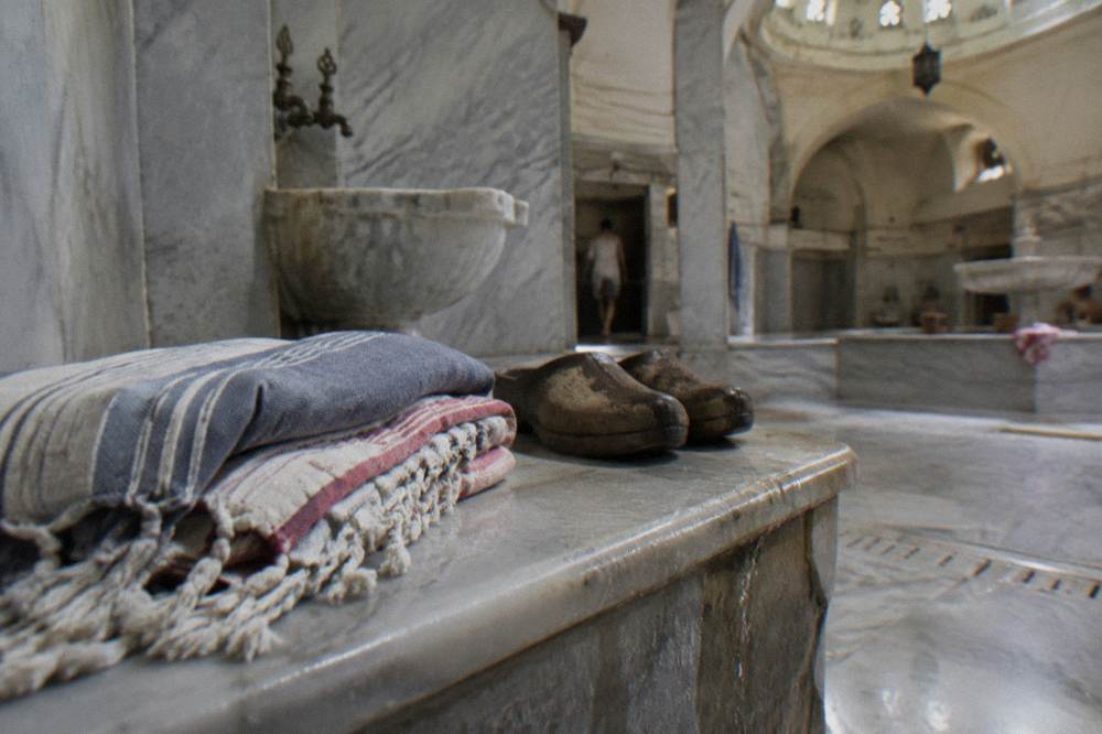 Folded cotton peshtemal wraps and wooden bath clogs on a marble bench