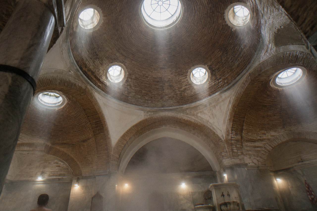Domed ceiling of an Ottoman hamam with round glass skylights above warm marble