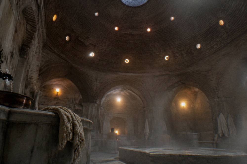 Domed ceiling of an Ottoman hamam with small round glass lights glowing in dim stone