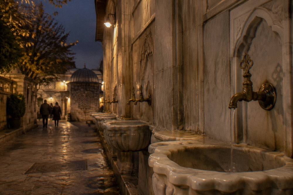 Warm light falling on marble basins and brass taps along the wall of an Ottoman bathhouse