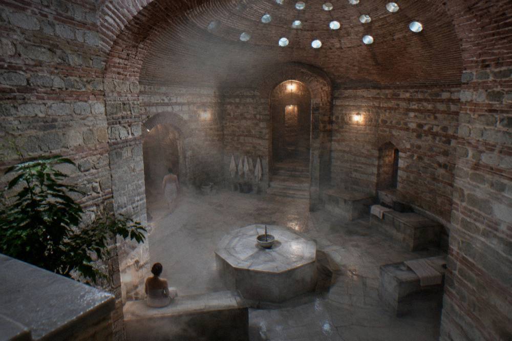 A stacked stone hamam interior with a domed ceiling pierced by small glass eyelets