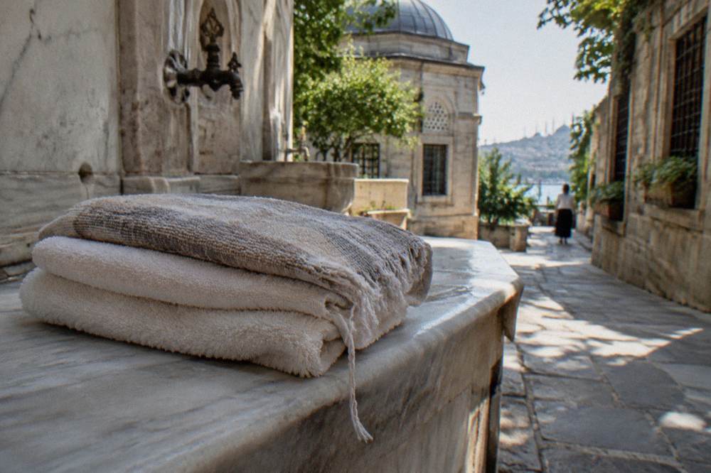 Folded cotton towels and a woven bath cloth stacked on a marble bench in warm light
