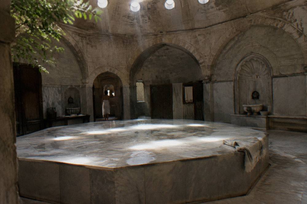 Warm marble göbektaşı platform under a stone dome pierced with small round skylights