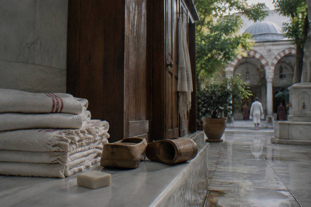 Stacked folded towels, wooden clogs and soap on a marble bench beside a changing cabin