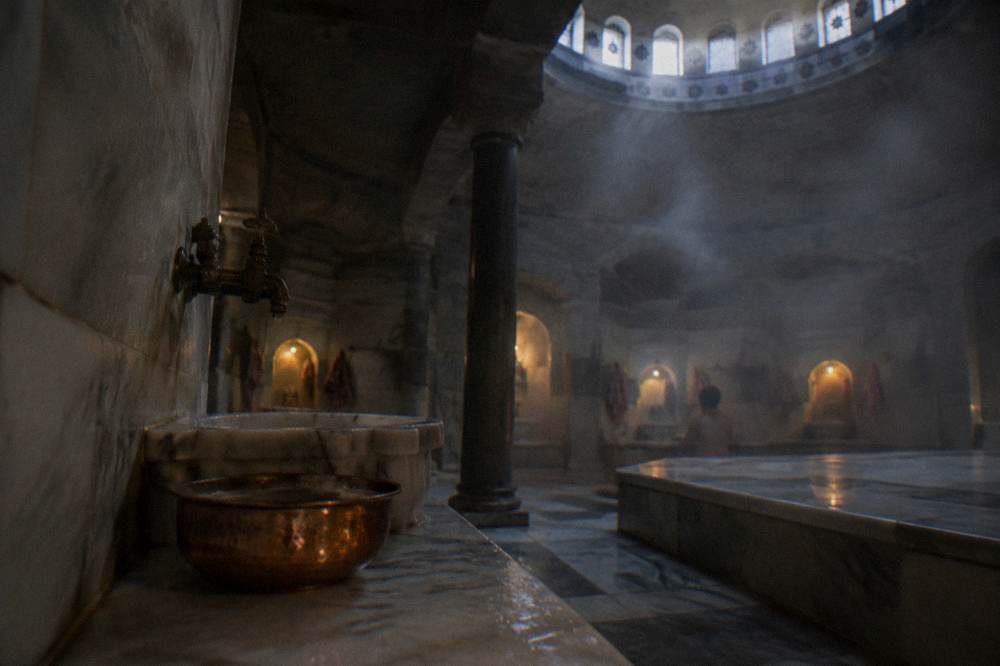 Copper bowl and steam beside a marble washing alcove inside a dimly lit domed bath