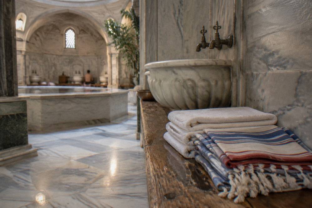 Stack of folded cotton towels and striped peshtemal cloths on a wooden bench beside a marble basin