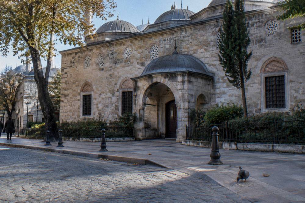 Sunlit stone exterior of a historic Istanbul bathhouse with a small domed entrance and arched windows
