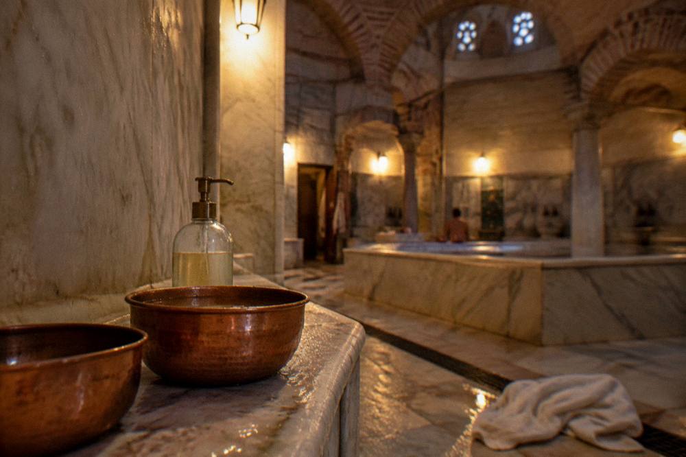 Copper bowls and soap bottles arranged on a marble ledge in a warm lamplit bathhouse corner