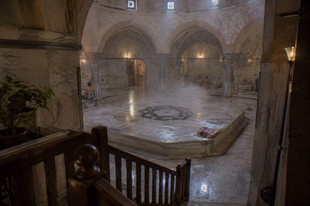 Warm marble interior of an Ottoman bathhouse with a raised stone platform under a domed ceiling