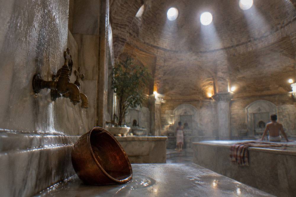 Stone domed ceiling of a Turkish bath with round glass skylights and steam in the light beams