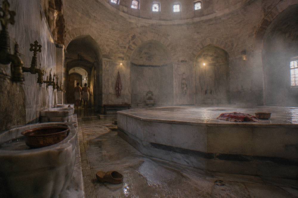 Warm marble interior of a domed Ottoman bath hall with a raised central stone platform and taps along the walls