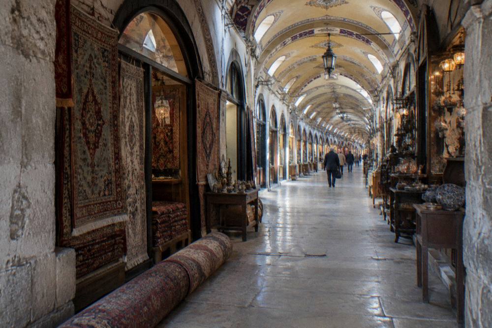 Arched stone entrance of a covered bazaar with lanterns and shopfronts along a vaulted passage