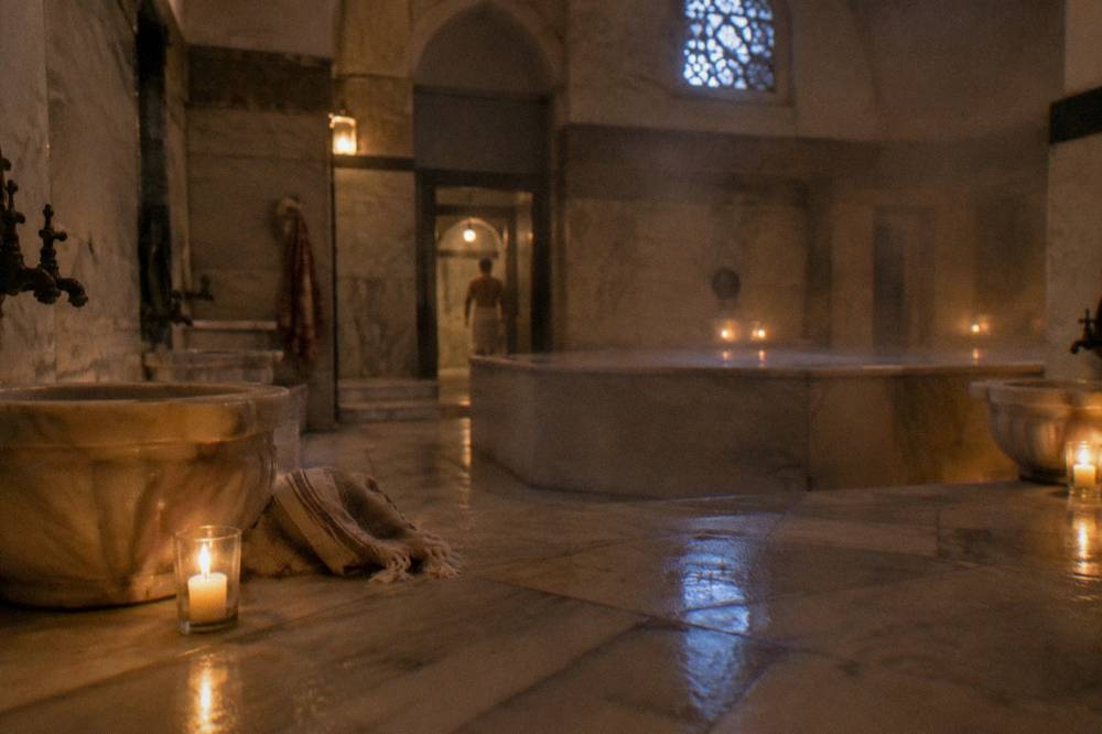 Candlelit marble hamam room with a central raised stone and steam in the air