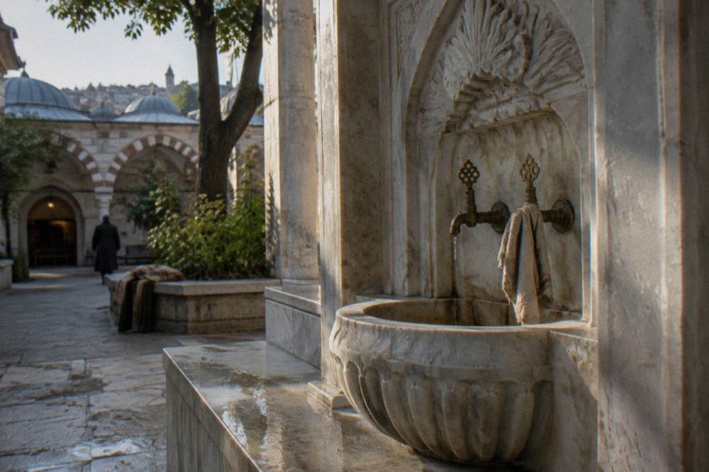 Ornate marble washing basin with brass taps along the wall of an Ottoman bathhouse