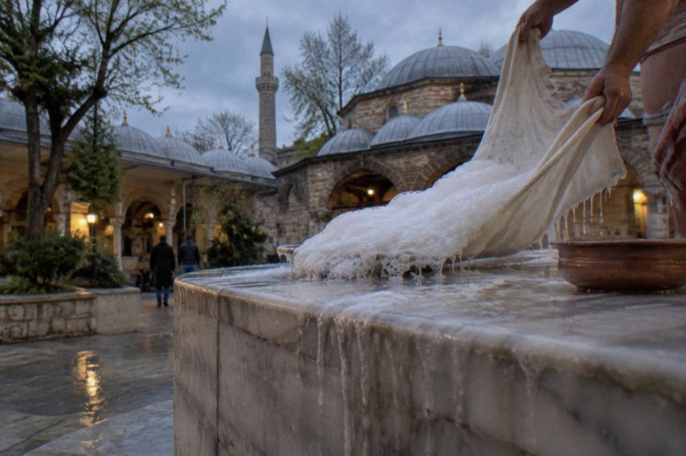 Dense white soap foam held in a cloth above a steamy marble hamam platform