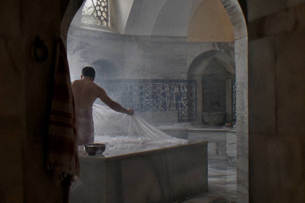 An attendant's cloth stretched taut and covered in fresh white soap foam inside a domed hamam hall