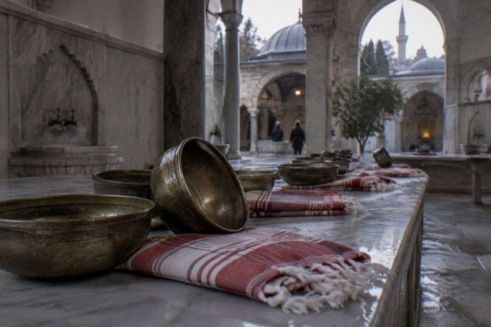 Rows of brass bathing bowls and folded striped peştemal cloths on a marble bench