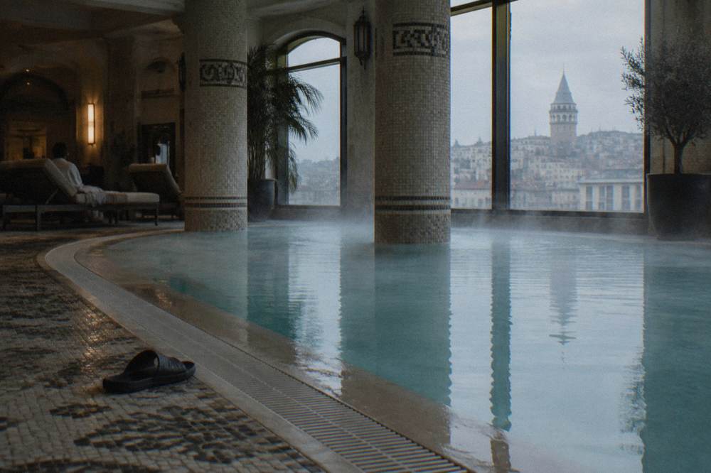 Lit indoor hotel pool with steam along the water edge and tiled columns