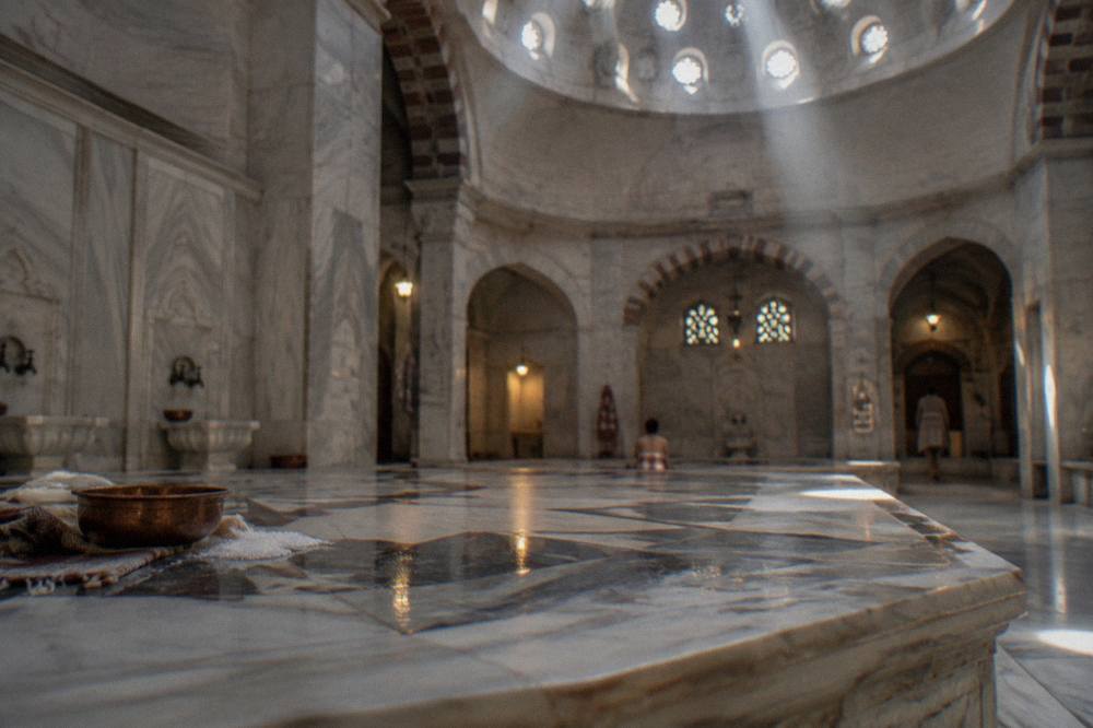 Warm marble göbektaşı platform in an Ottoman hamam lit by small domed roof windows