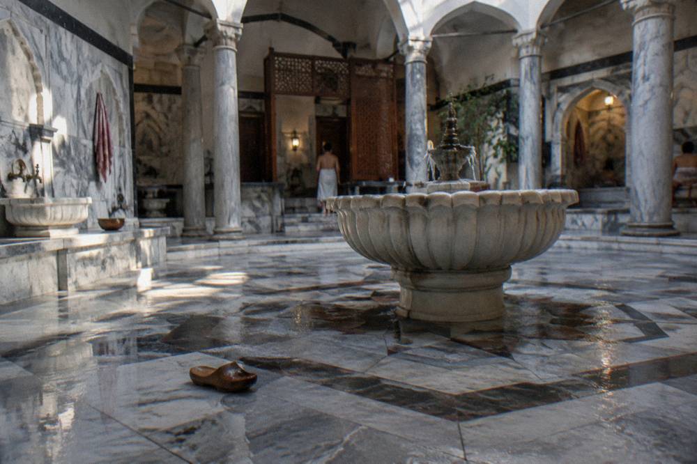 Ornate hamam interior with patterned marble floors and a carved stone fountain basin