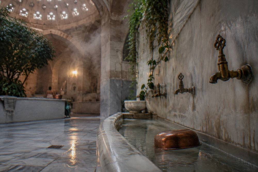 Steam rising in a domed hamam hot room with marble basins along the wall