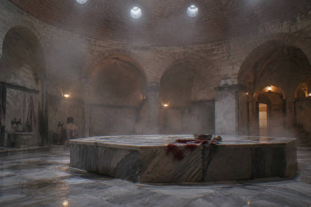 Steam rising in a domed hamam hot room with a broad heated marble platform and small round ceiling lights