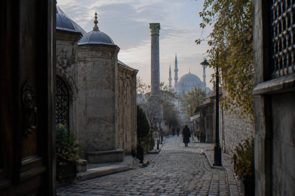 Narrow old city street in Istanbul with stone buildings and a distant mosque dome in soft morning light