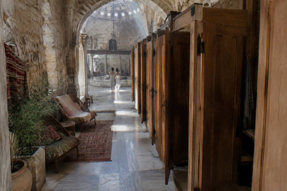 Traditional hammam changing cubicles with wooden doors, rattan loungers and patterned textiles along a stone wall