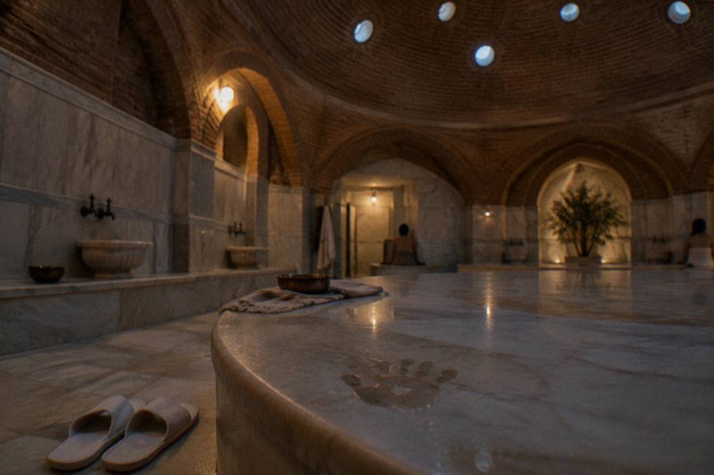 Warm marble göbektaşı platform inside a domed hamam lit by small glass circles set into the ceiling