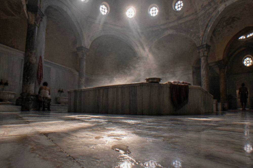 Sunlight through round dome windows falling on the steam and marble floor of a quiet hamam hall